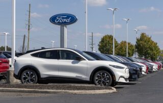 White Ford Mach E in front of a Ford logo