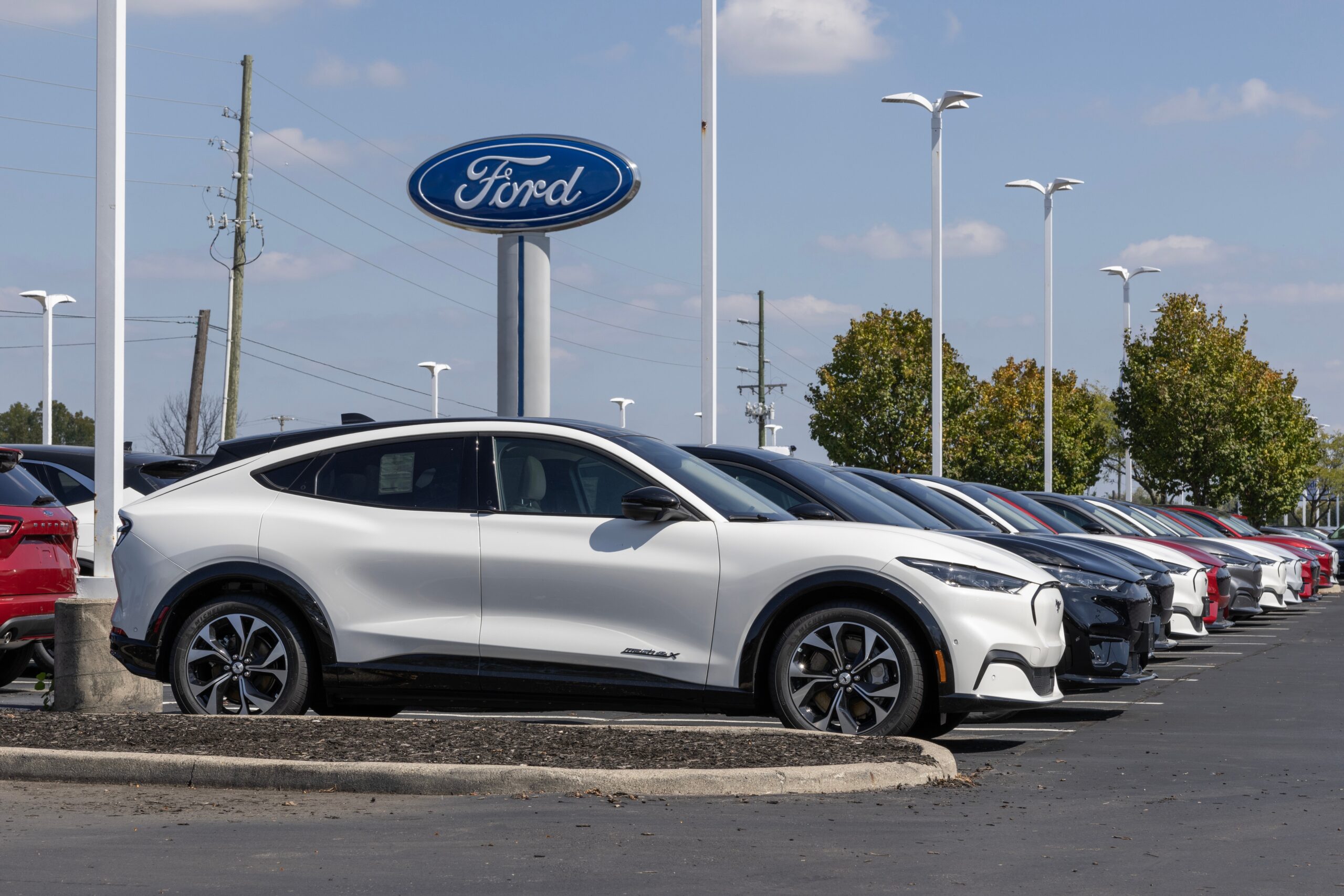 White Ford Mach E in front of a Ford logo