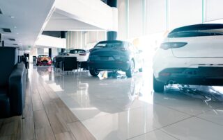 A bright, modern car dealership showroom in 2026 featuring a row of well-maintained used cars from the 2021-2023 model years. The sleek white and blue SUVs are positioned on a polished tile floor, highlighting the premium quality and modern features available at used-market prices.