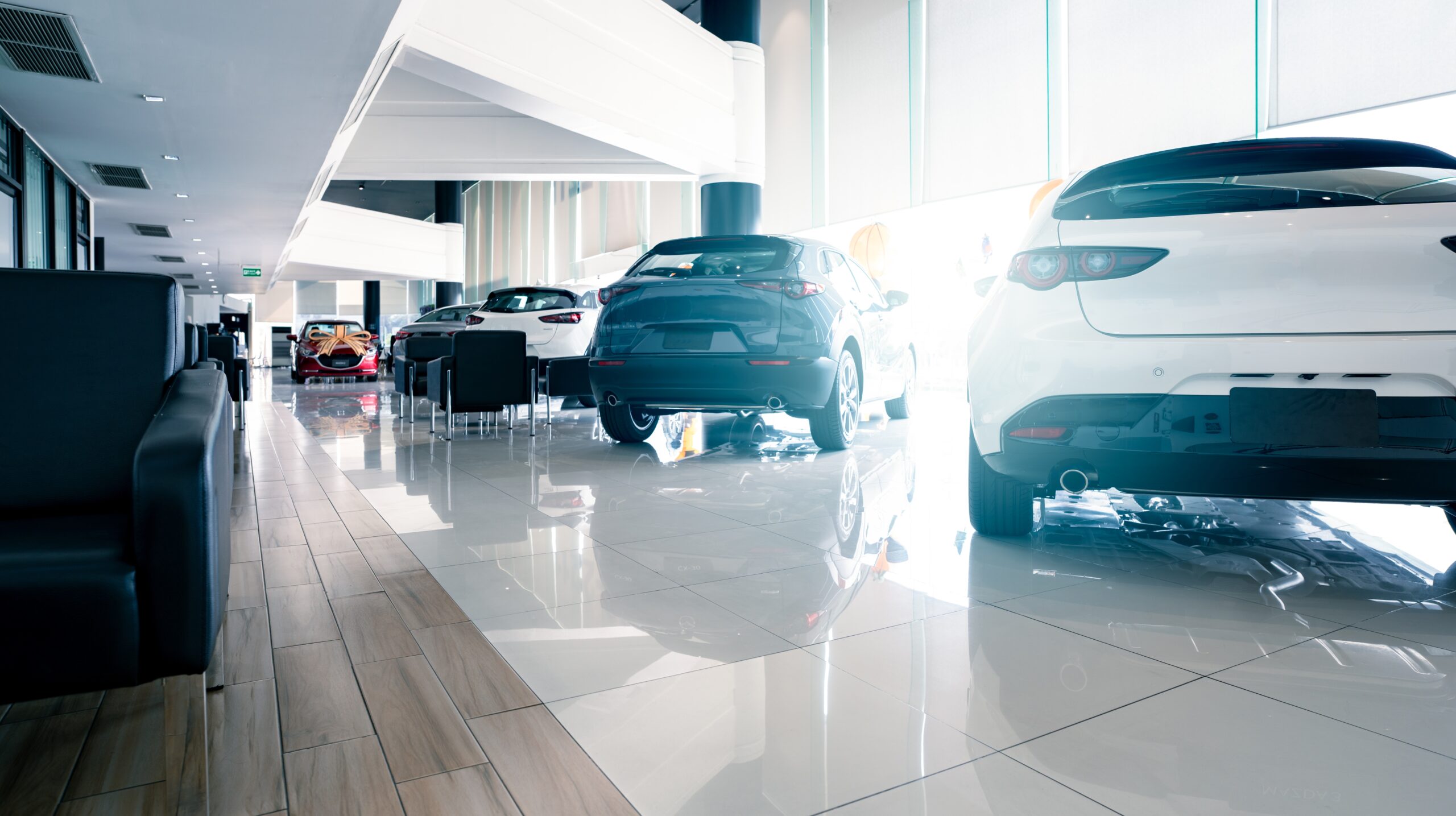 A bright, modern car dealership showroom in 2026 featuring a row of well-maintained used cars from the 2021-2023 model years. The sleek white and blue SUVs are positioned on a polished tile floor, highlighting the premium quality and modern features available at used-market prices.
