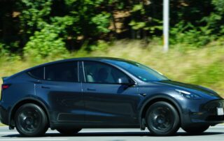 Side profile view of a dark metallic grey Tesla Model Y driving fast on an open road, representing the range and performance of pre-owned electric SUVs.