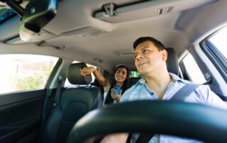 Rideshare driver steering a used vehicle while a female passenger points for directions from the back seat.