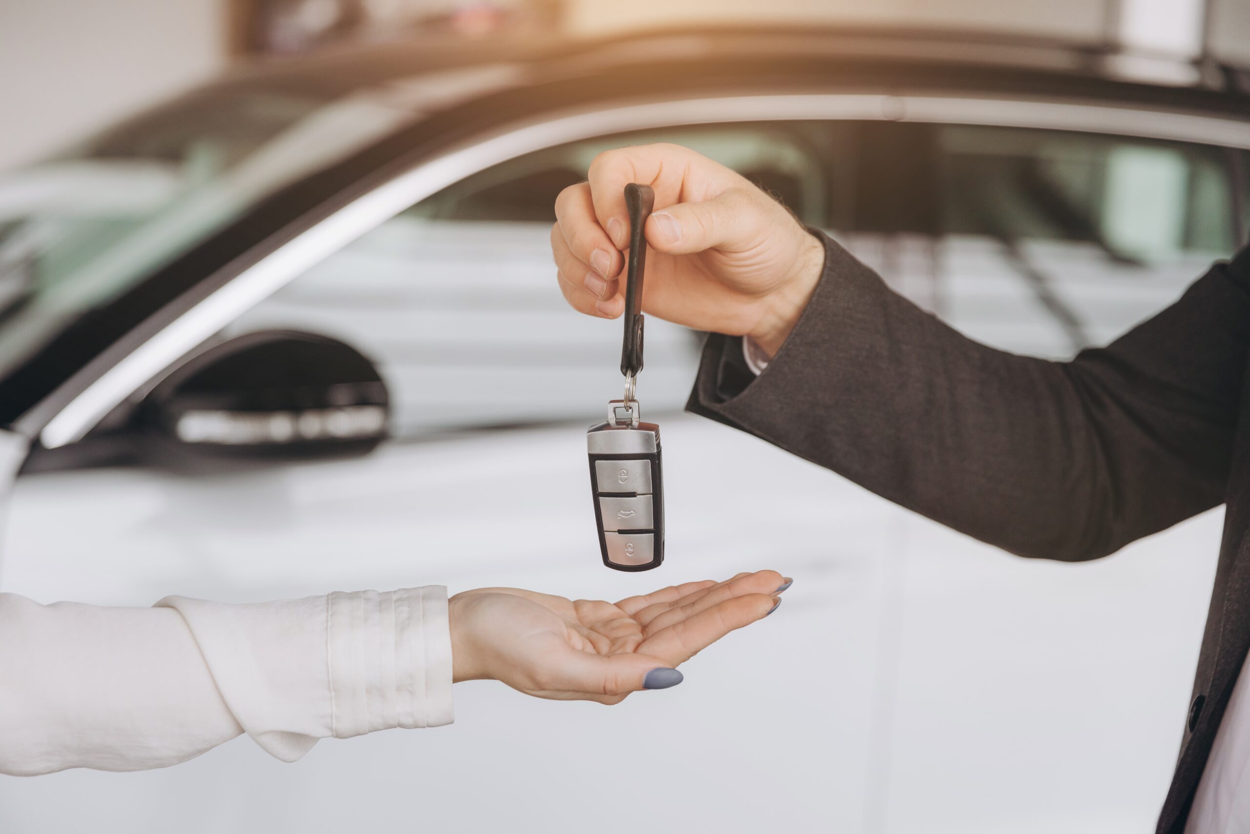 Car dealer handing over a key fob to a customer's open hand in front of a white vehicle.