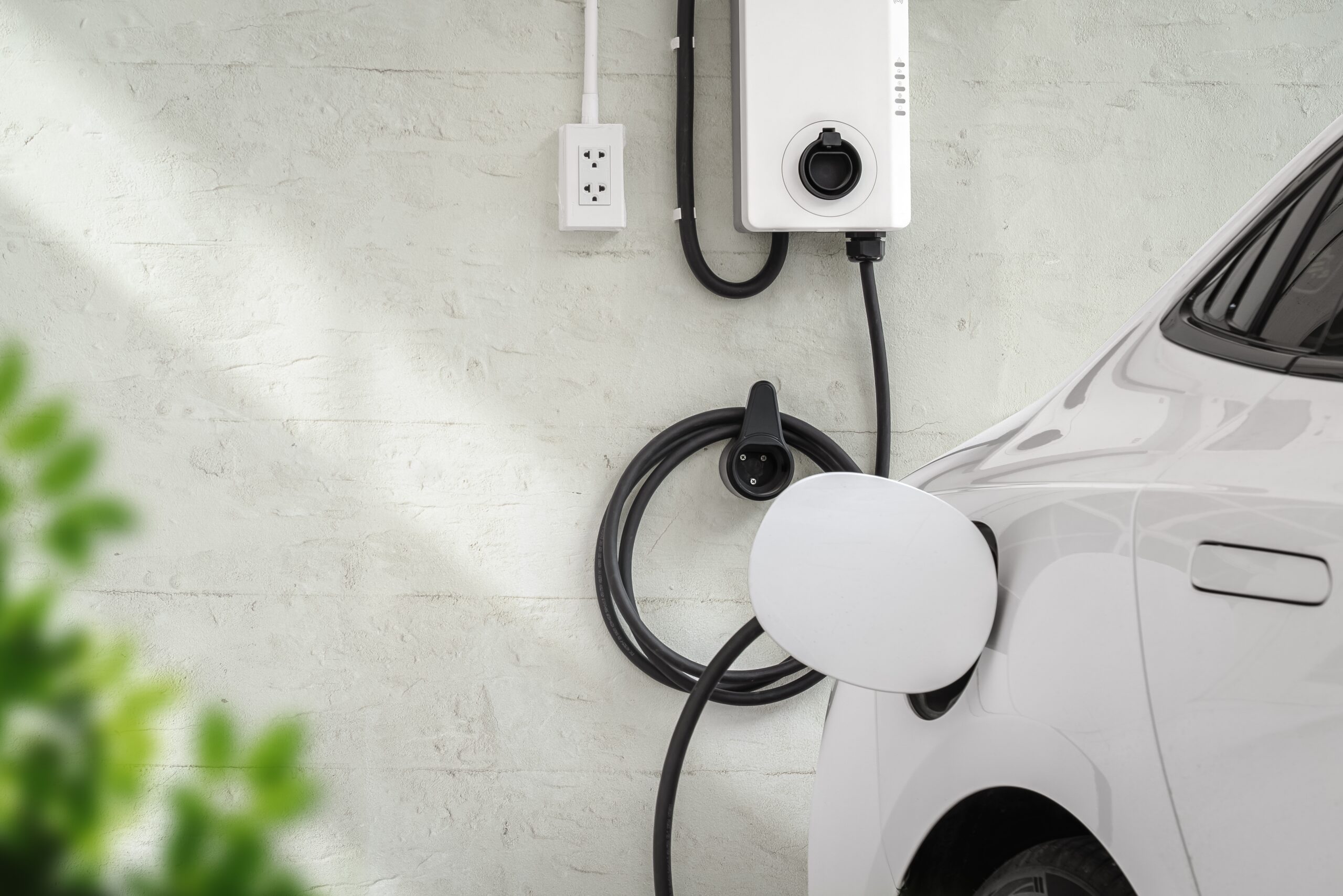Wall-mounted Level 2 EV charger station installed on a garage wall charging a white electric vehicle.