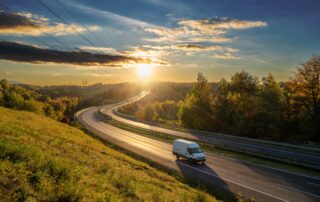White cargo van driving on a highway through a scenic rural countryside at sunset.